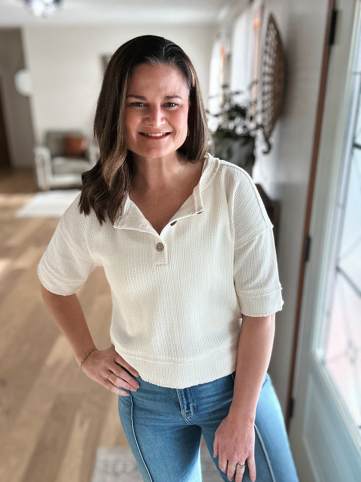 Woman wearing a white short-sleeve shirt and blue jeans indoors.