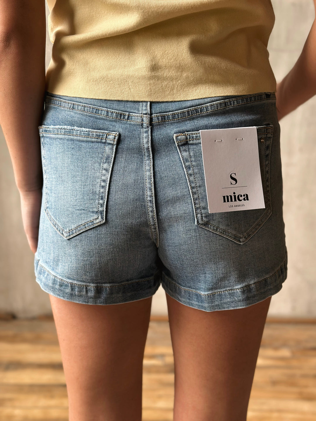 Person wearing blue denim shorts with a brand tag on a neutral background