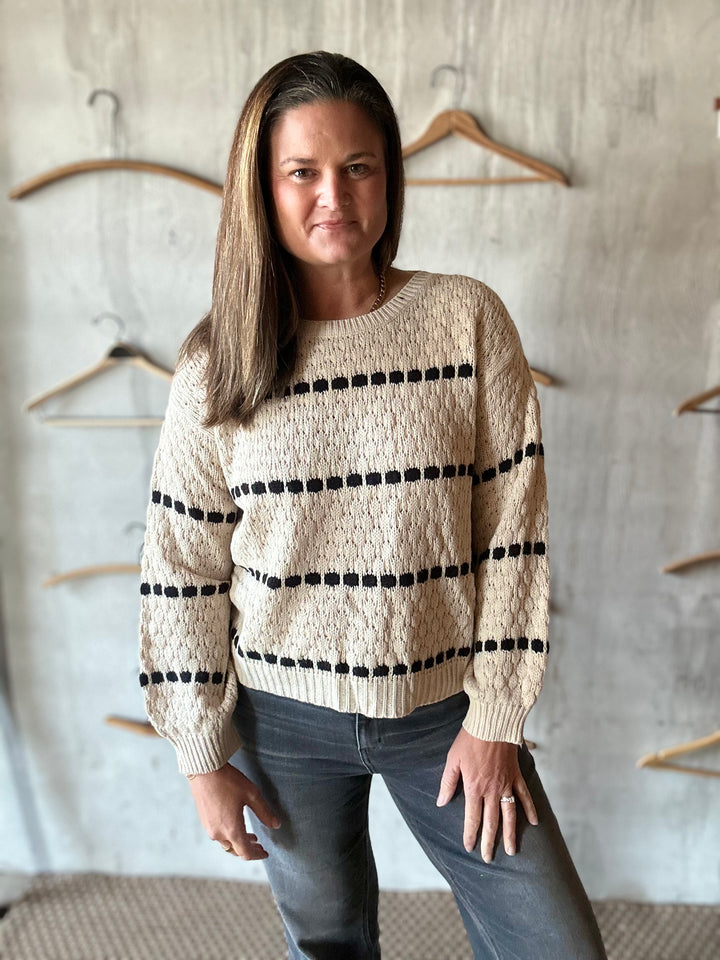 Woman wearing a cream crewneck sweater with black bobble stripes and jeans