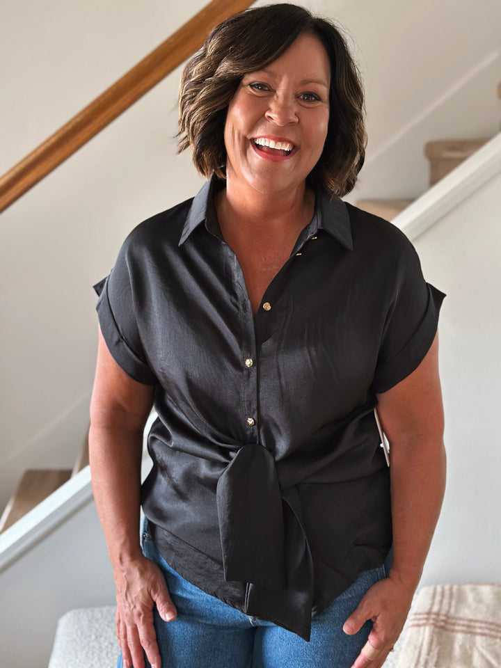 Woman wearing a black shirt with a tie front standing indoors.
