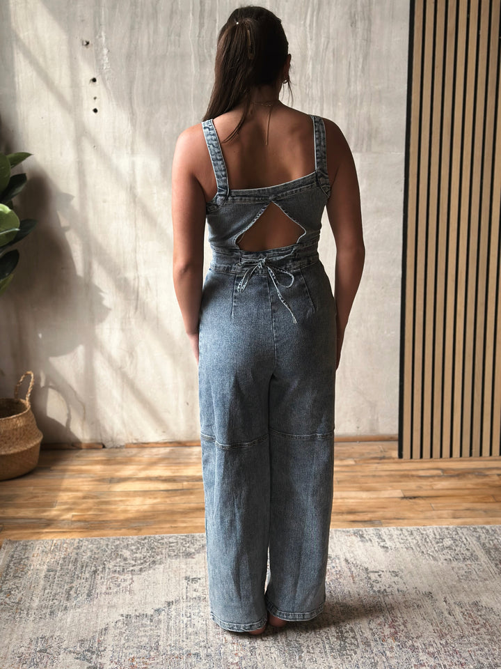 Person wearing a denim jumpsuit with cut-out back design indoors.