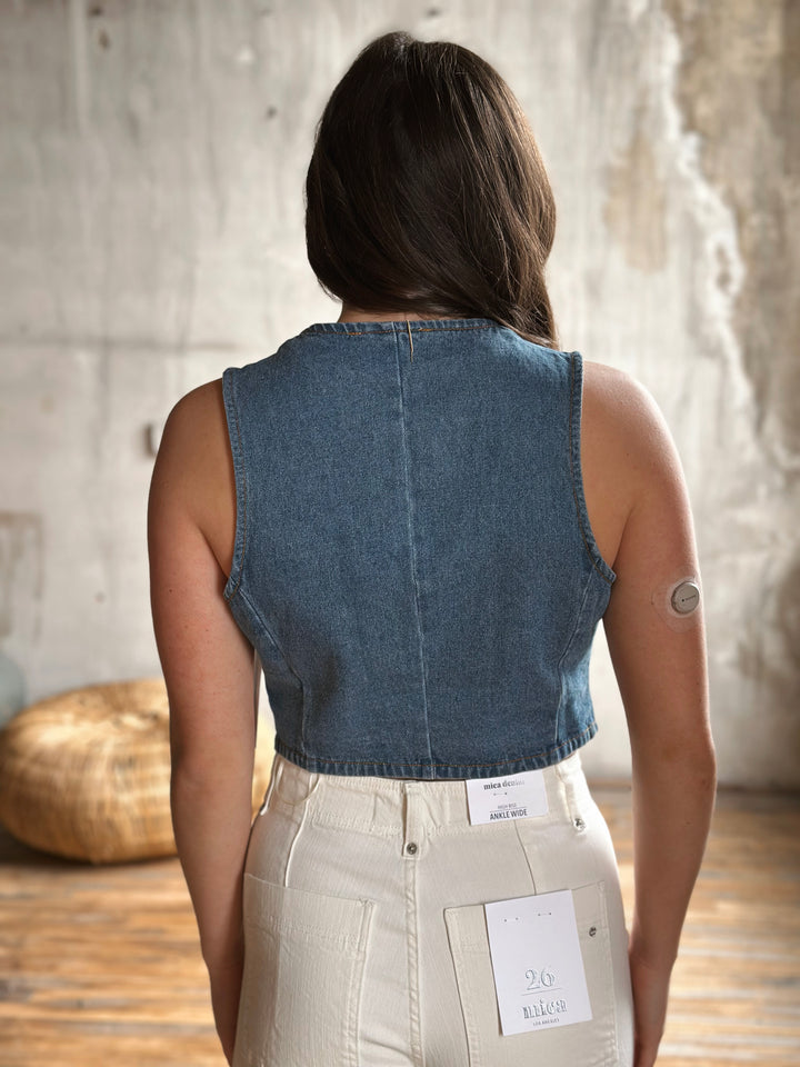 Person wearing a denim vest and beige pants with a neutral background