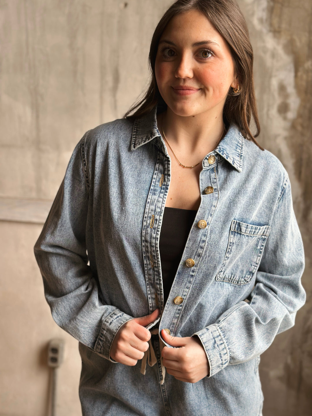 Woman wearing a light blue denim jacket indoors against a neutral background