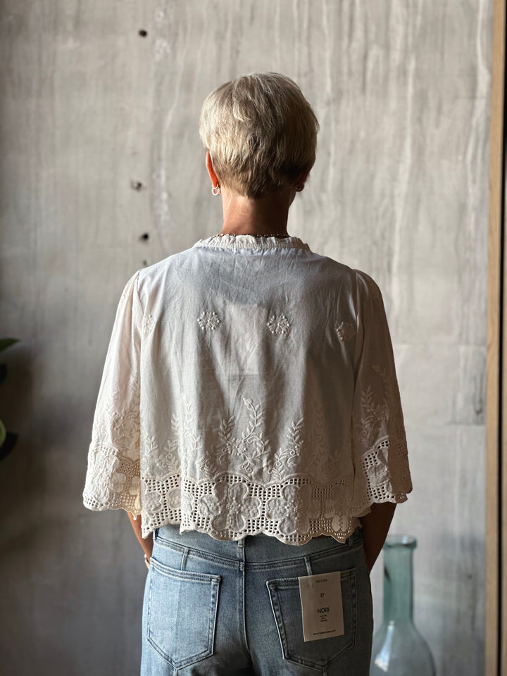 Person wearing a light-colored embroidered blouse with a plain background