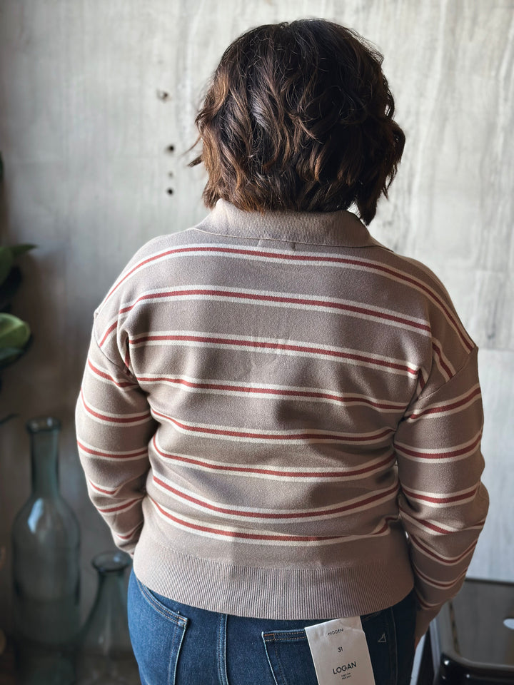 Person wearing a striped sweater with a visible tag, standing in a room with a textured wall.