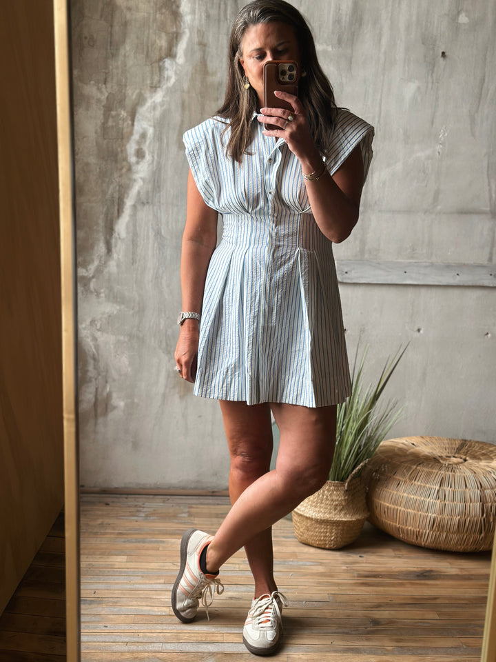 Woman taking a mirror selfie wearing a striped dress in a room with a textured wall and wooden floor.