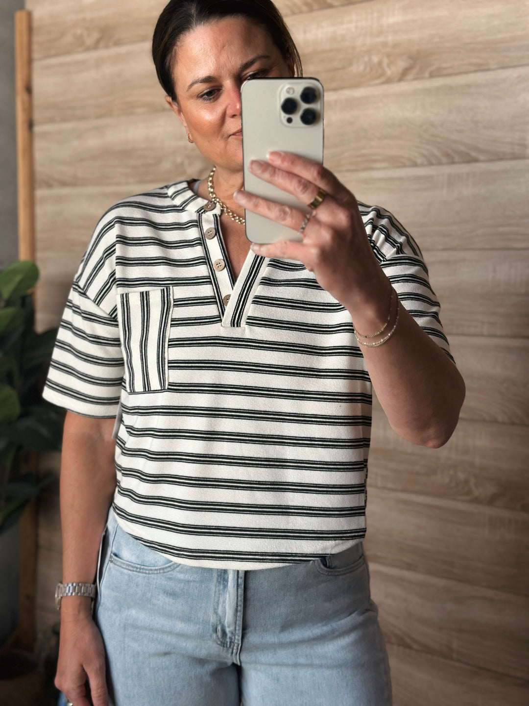 A woman wearing a short sleeved black and white striped v-neck shirt with buttons. With a pocket on the left side of the shirt. 