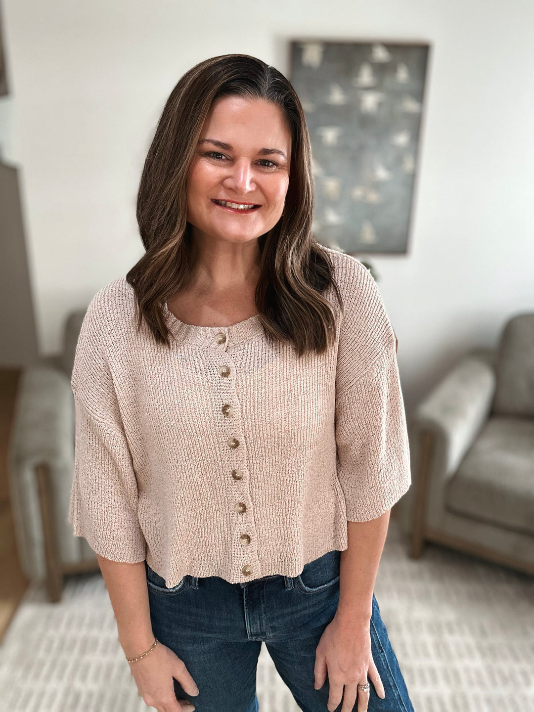 Woman wearing a beige cardigan in a living room setting