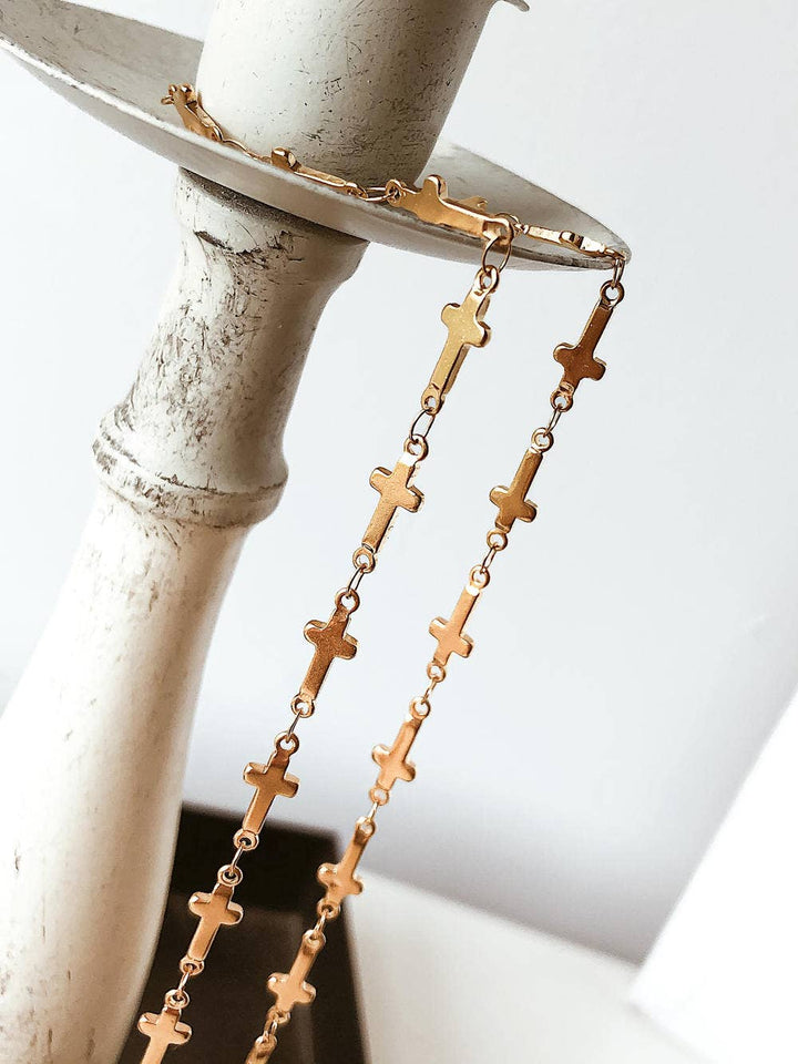 Gold cross necklace on a white pedestal