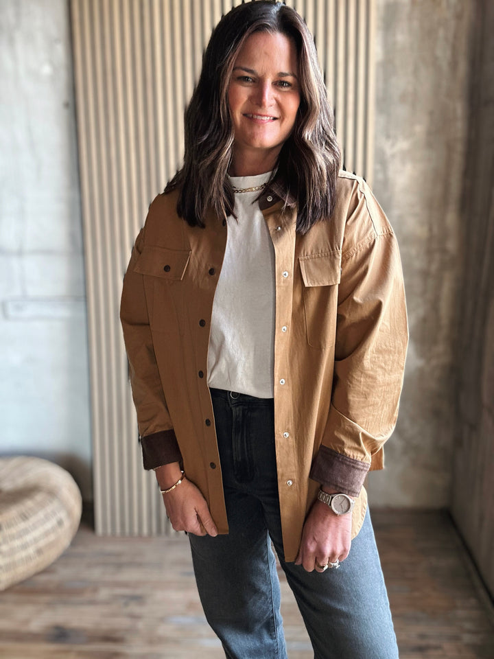 Woman wearing a beige jacket over a white shirt and blue jeans in an indoor setting.
