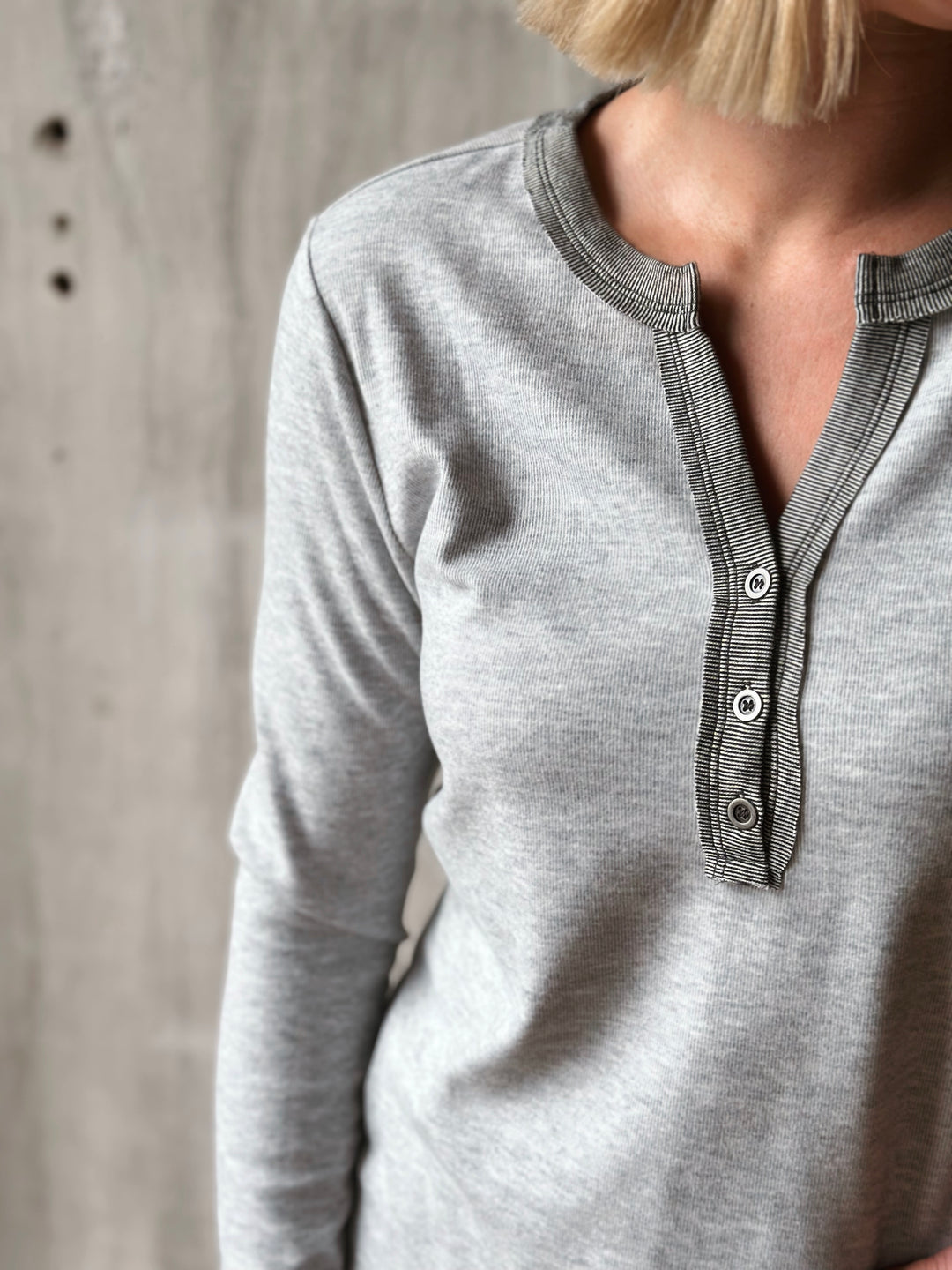 Gray long-sleeve shirt with button details worn by a person against a neutral background