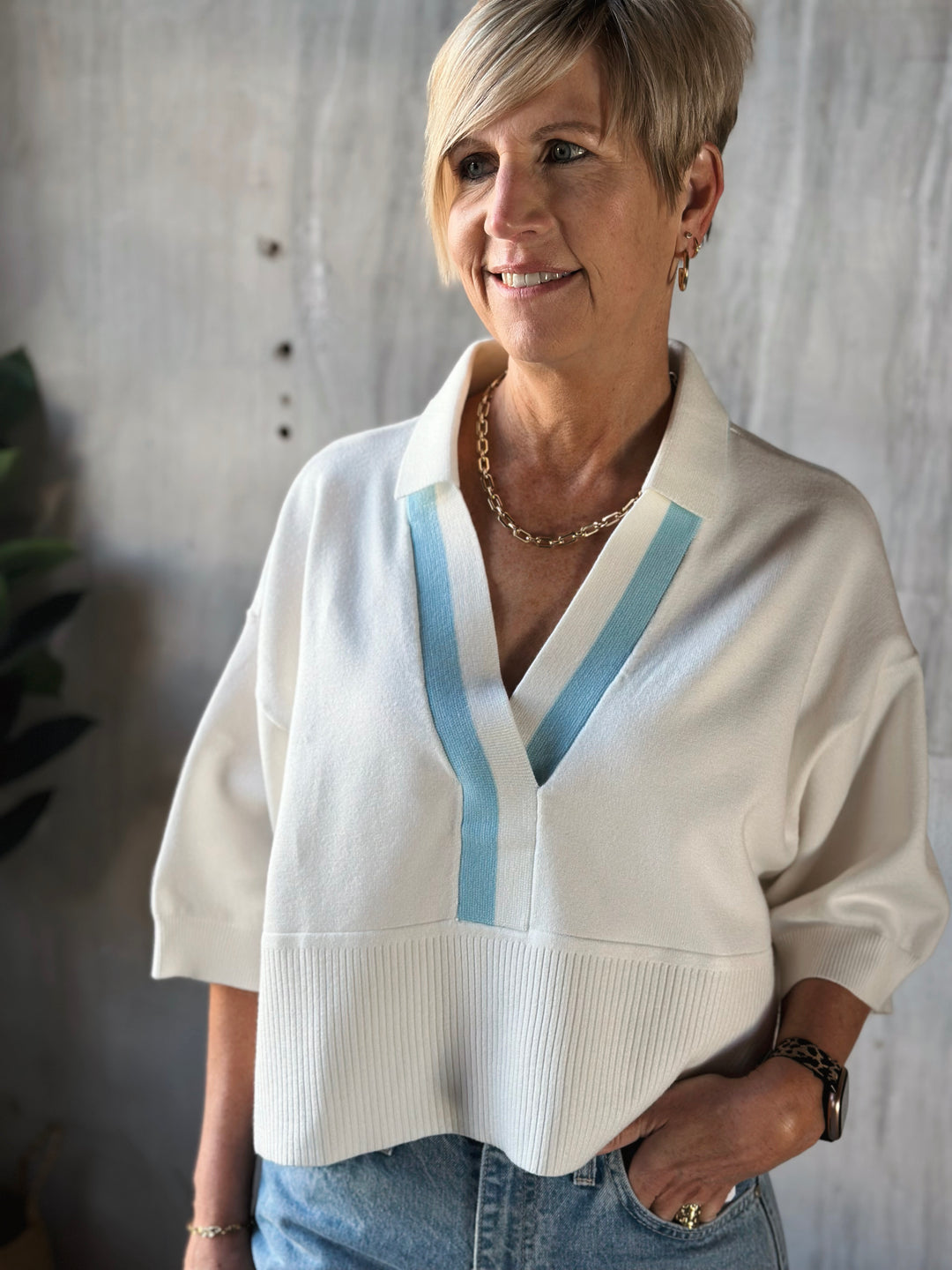 Woman wearing a white sweater with blue accents against a neutral background