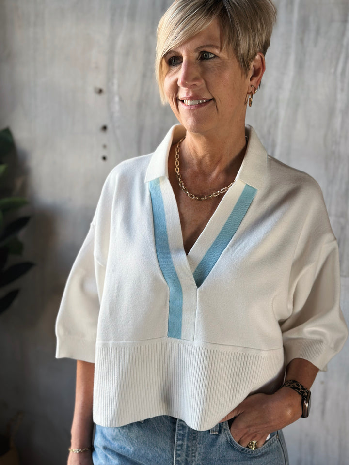 Woman wearing a white sweater with blue accents against a neutral background