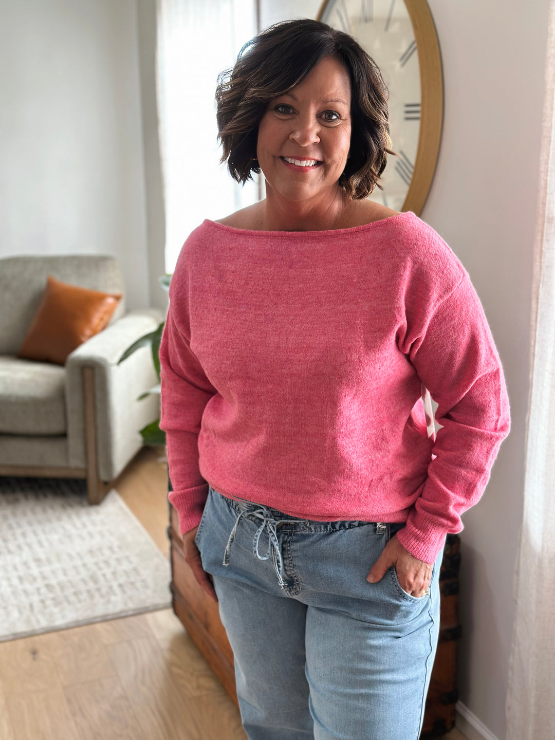 Woman wearing a pink sweater and blue jeans standing in a living room.