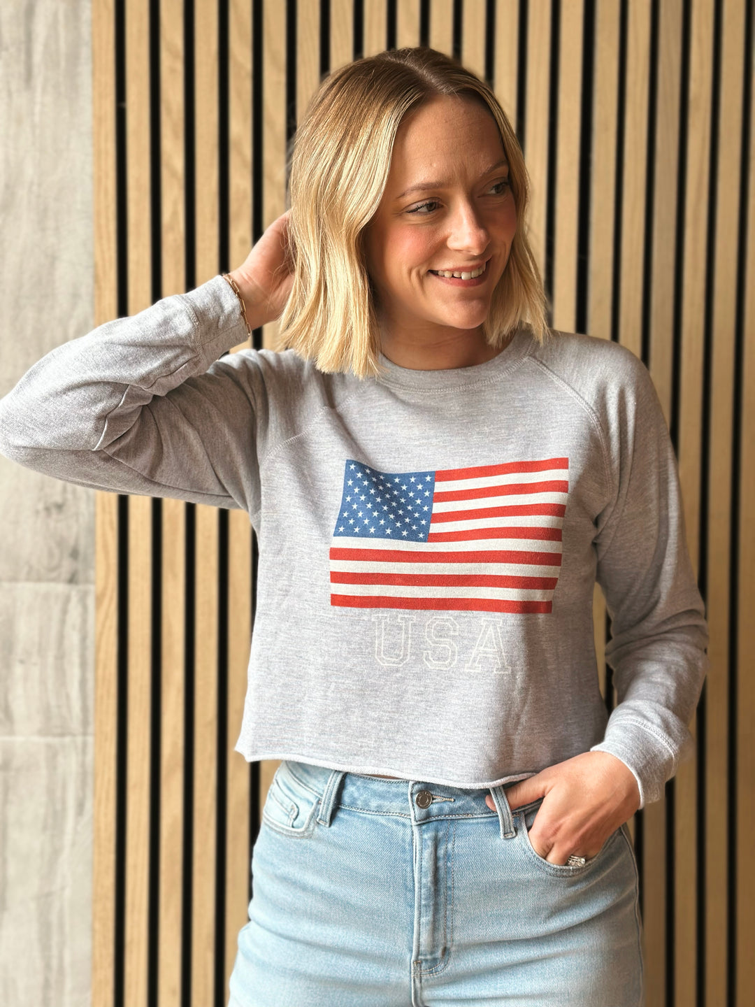 Woman wearing a gray sweatshirt with an American flag design against a wooden panel background