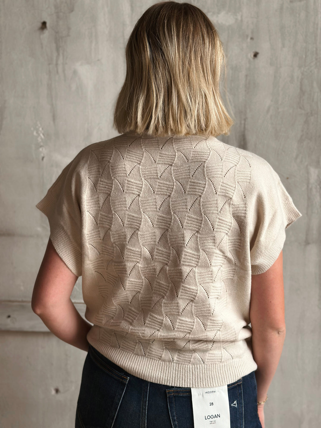 Person wearing a beige patterned sweater with a concrete wall background