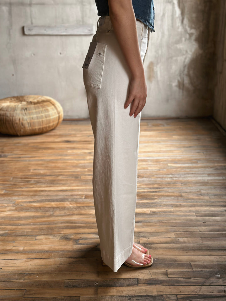 Person wearing white jeans standing on a wooden floor with a neutral background