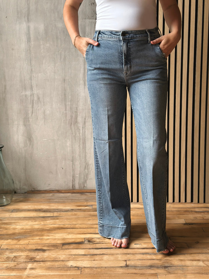 Person wearing blue jeans standing on a wooden floor with a neutral wall background