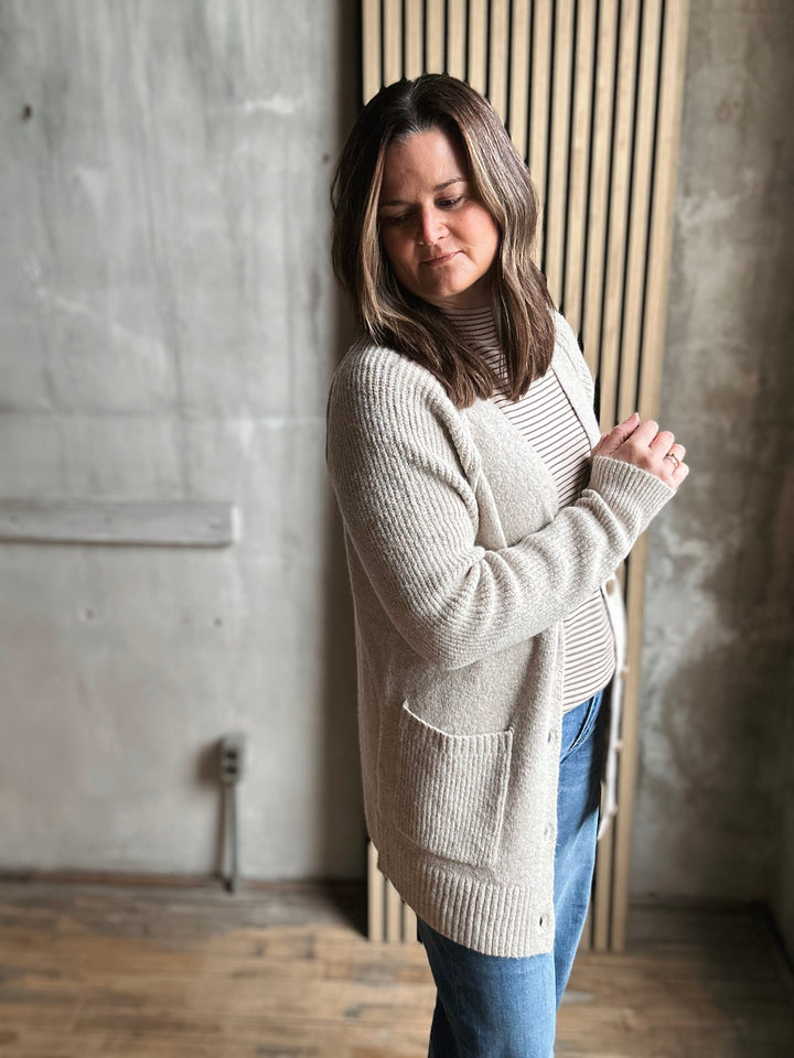 Woman wearing a light gray sweater and blue jeans against a concrete wall.
