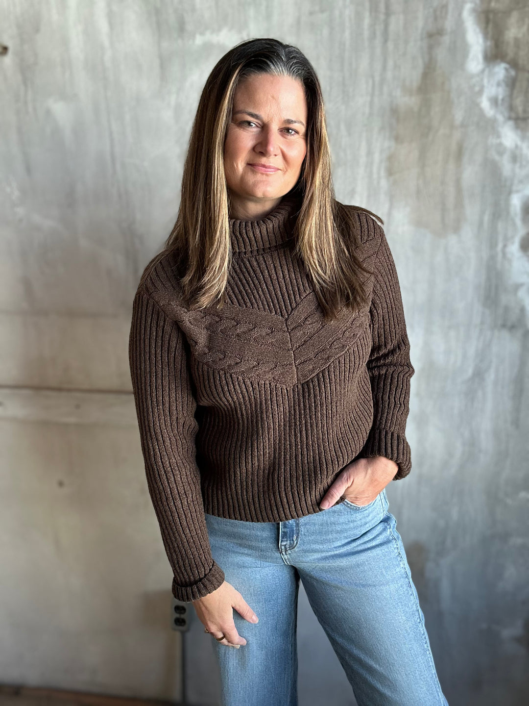 Woman wearing a chocolate brown turtleneck sweater with light-wash jeans