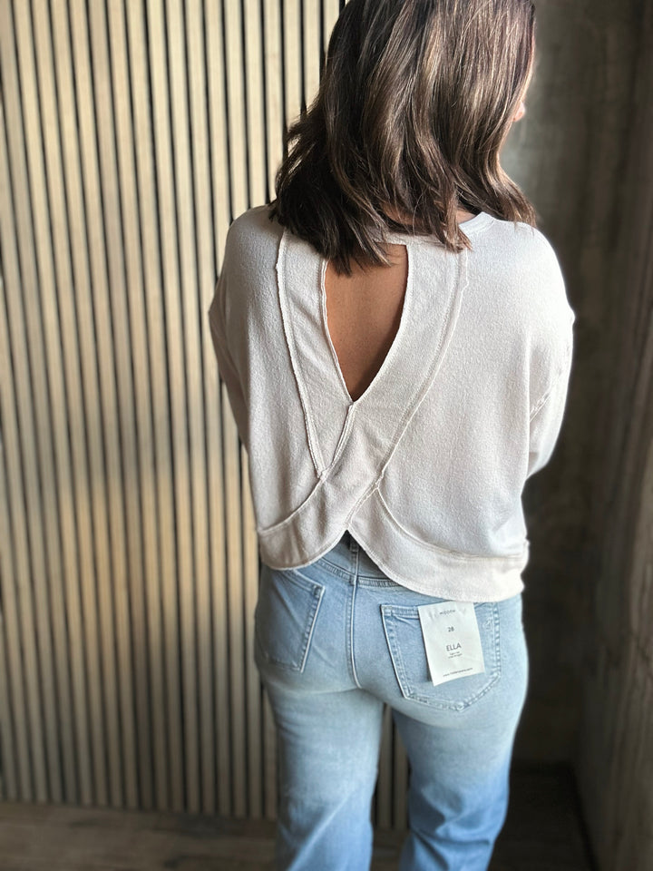Person wearing a white open-back top and light blue jeans with a visible brand tag, standing against a striped wall.