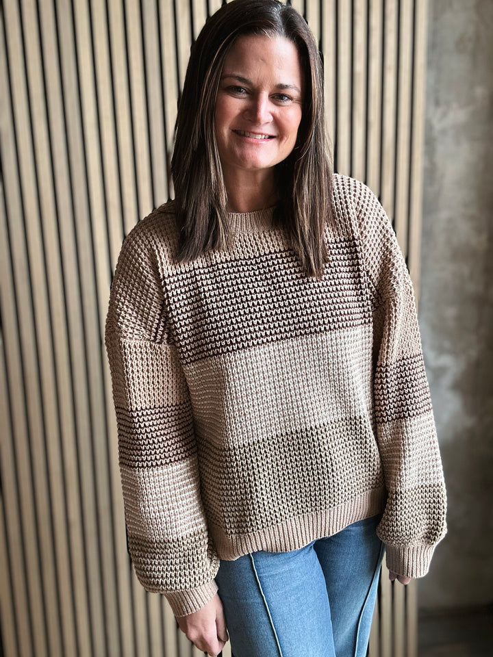 Woman wearing a beige knitted sweater standing against a textured wall.