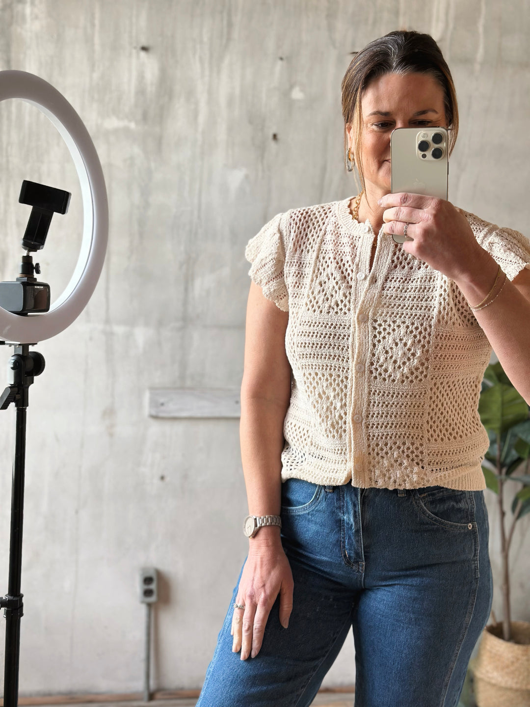 Woman taking a mirror selfie wearing a beige crochet top and blue jeans.