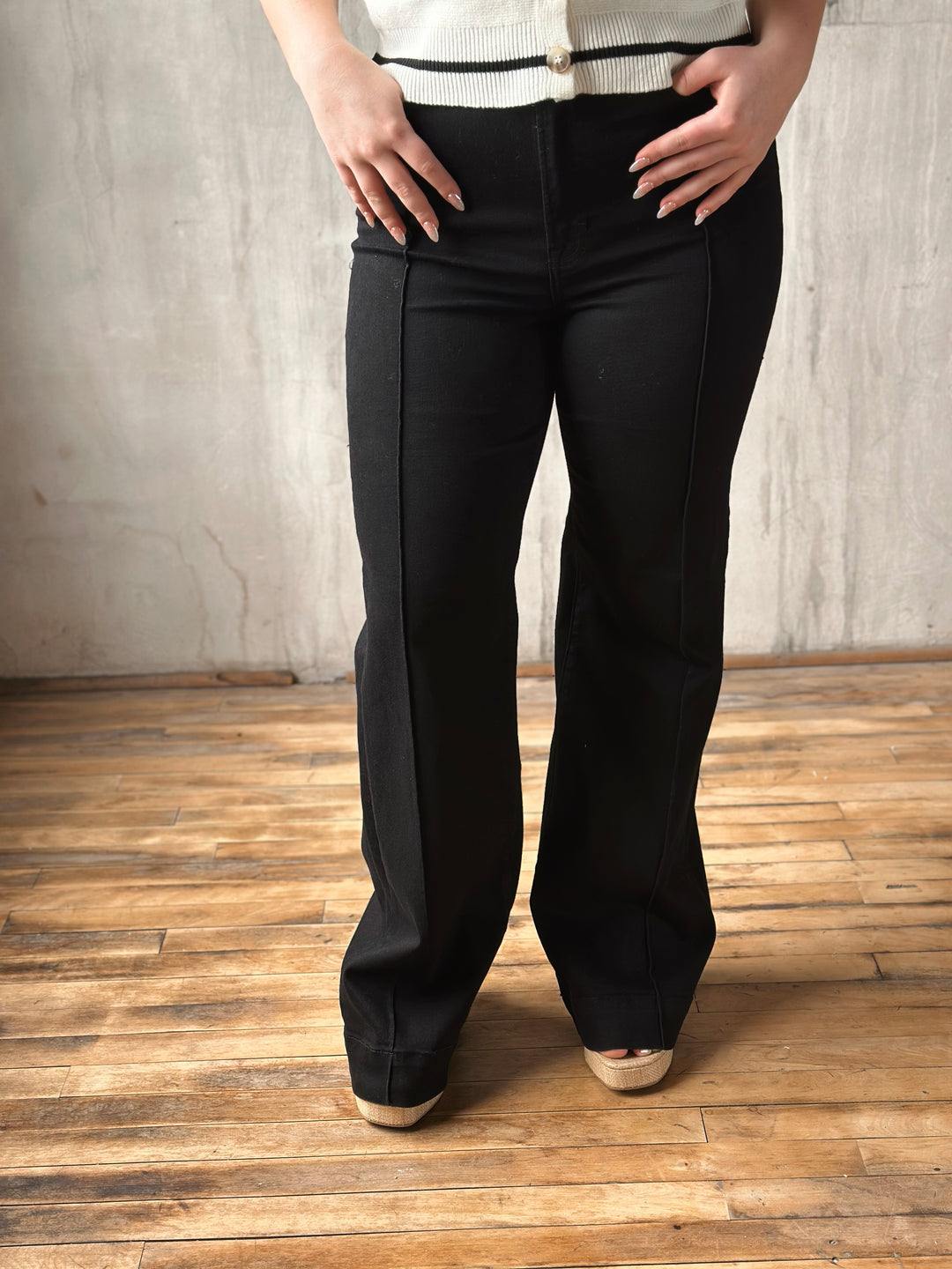 Person wearing black flared pants on a wooden floor with a gray wall background