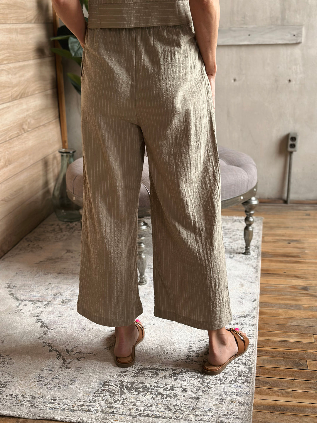 A person wearing sage wide-leg pants standing in a room with a wooden floor and light-colored walls.