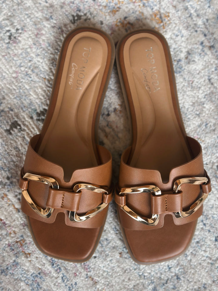 Pair of brown sandals with gold buckles on a textured surface.