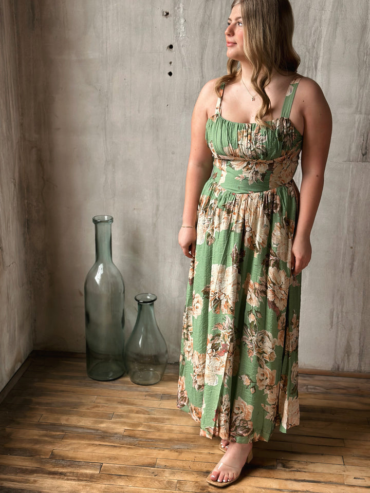 Woman wearing a floral dress standing in a room with textured walls and wooden floor.