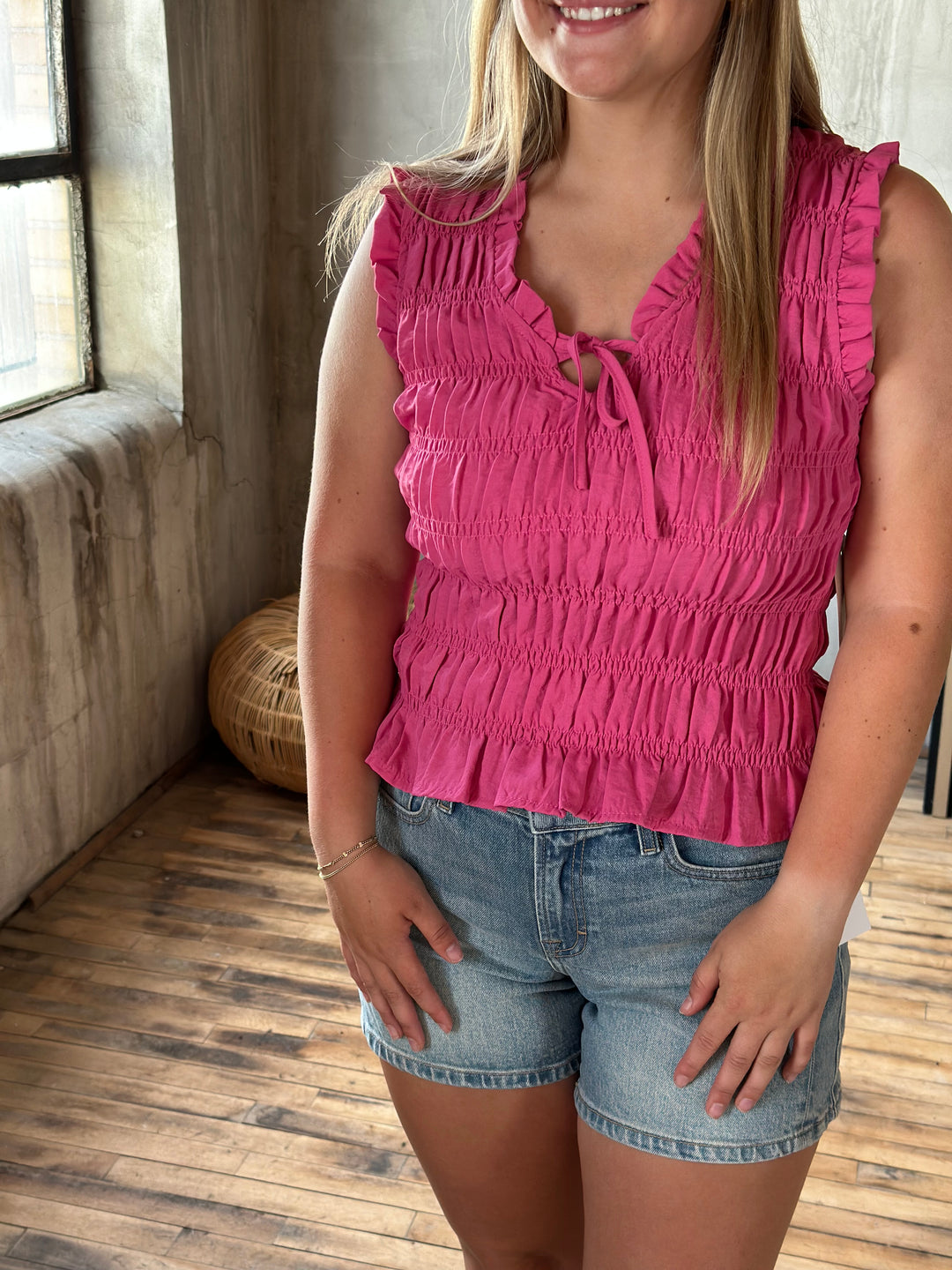 A person wearing a pink ruffle and sleeveless top and denim shorts on a wooden floor.