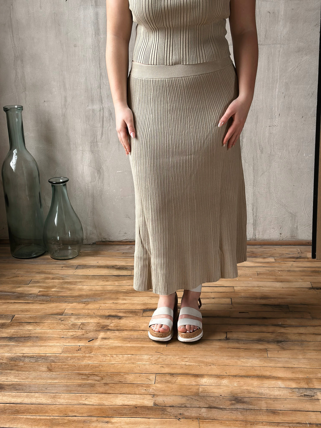 Person wearing a beige ribbed skirt standing on a wooden floor with a neutral background