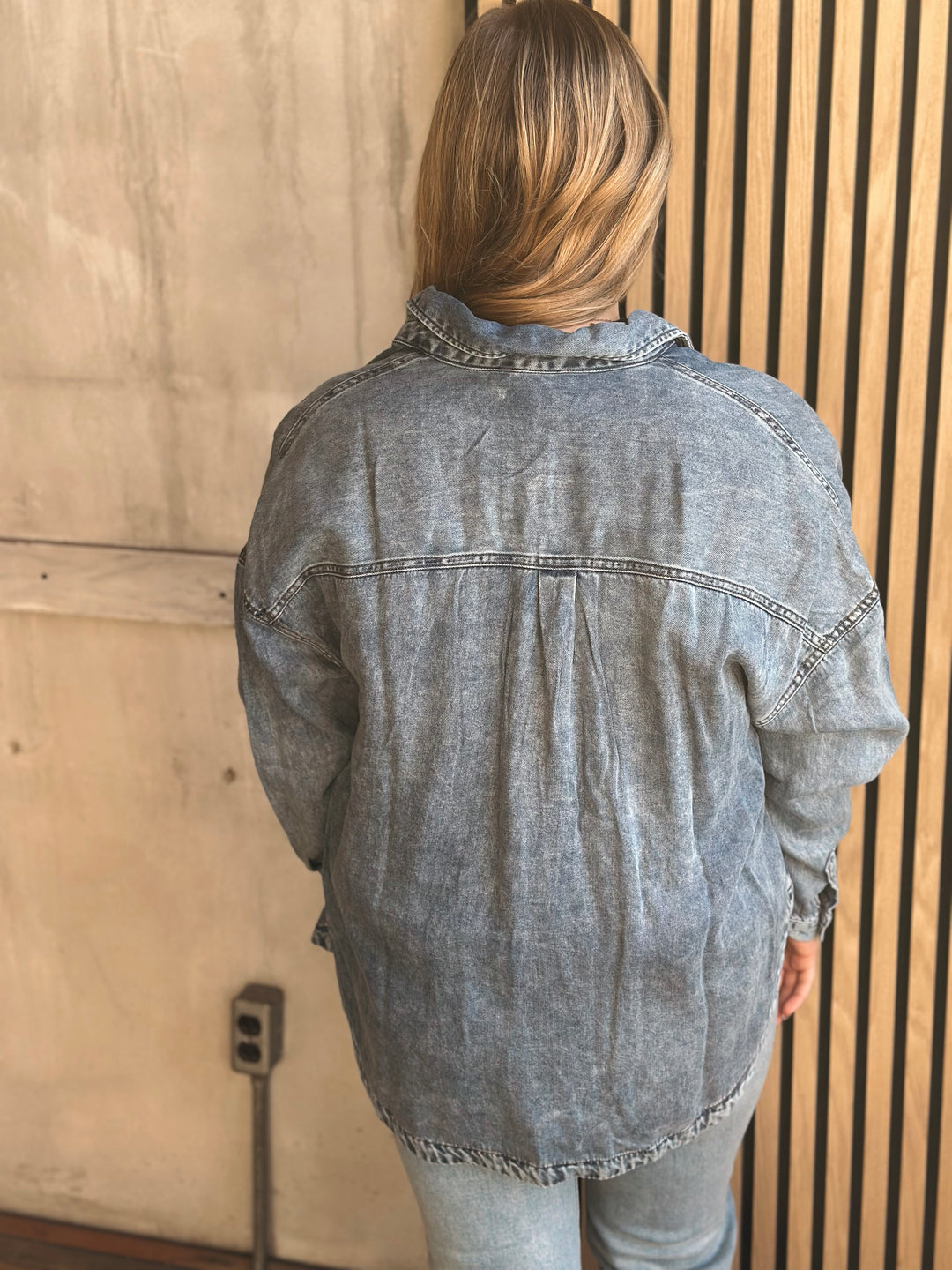 Person wearing a denim jacket standing against a wooden wall.