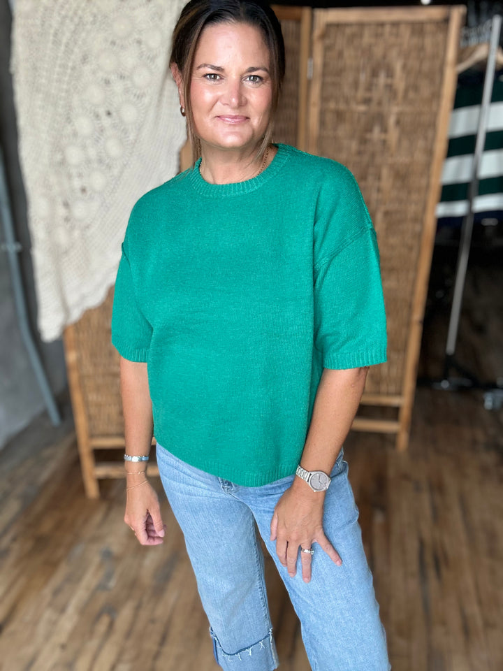 A woman wearing a vibrant green short-sleeve knit sweater and light blue jeans.