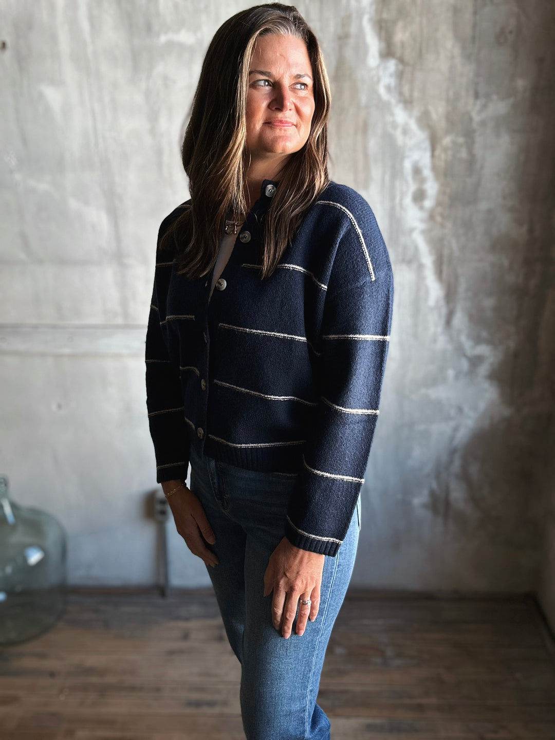 Woman wearing a navy striped sweater and jeans standing against a textured wall.