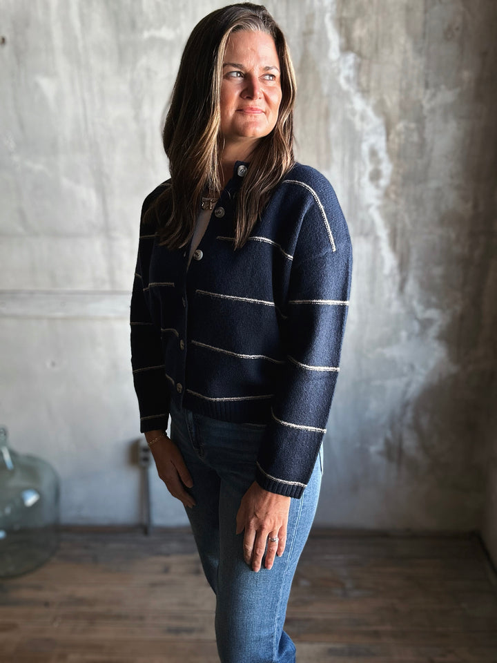 Woman wearing a navy striped sweater and jeans standing against a textured wall.