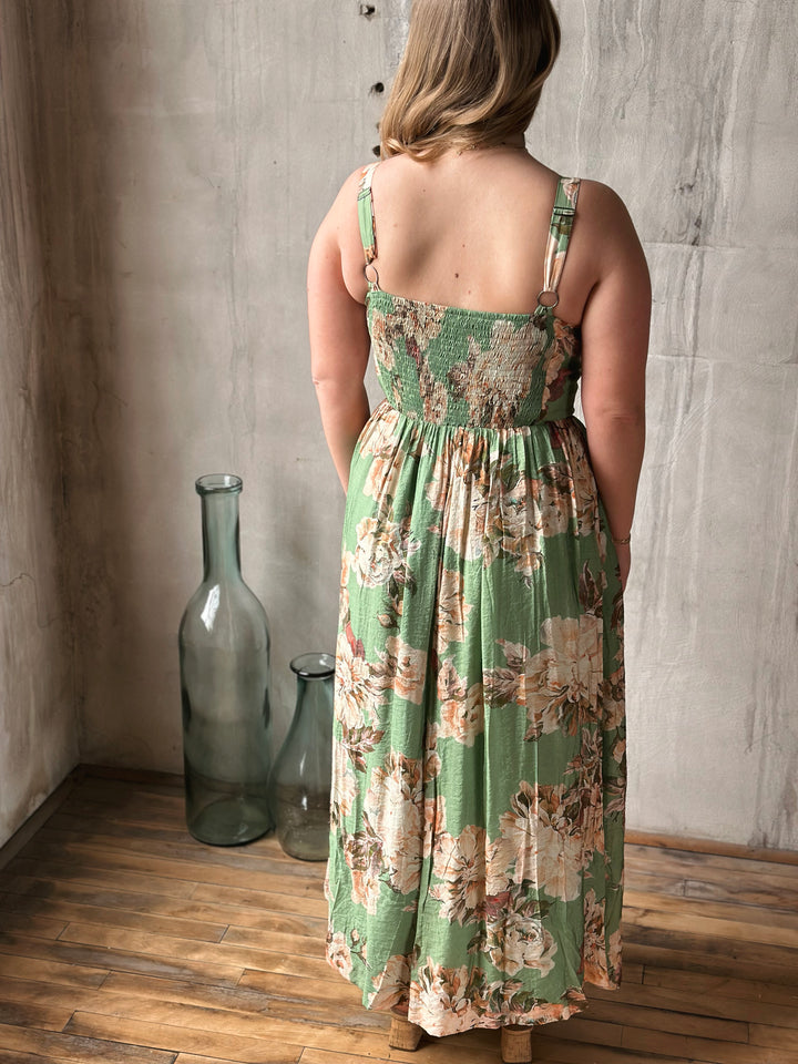 Woman wearing a green floral dress standing in a room with wooden floor and textured walls.