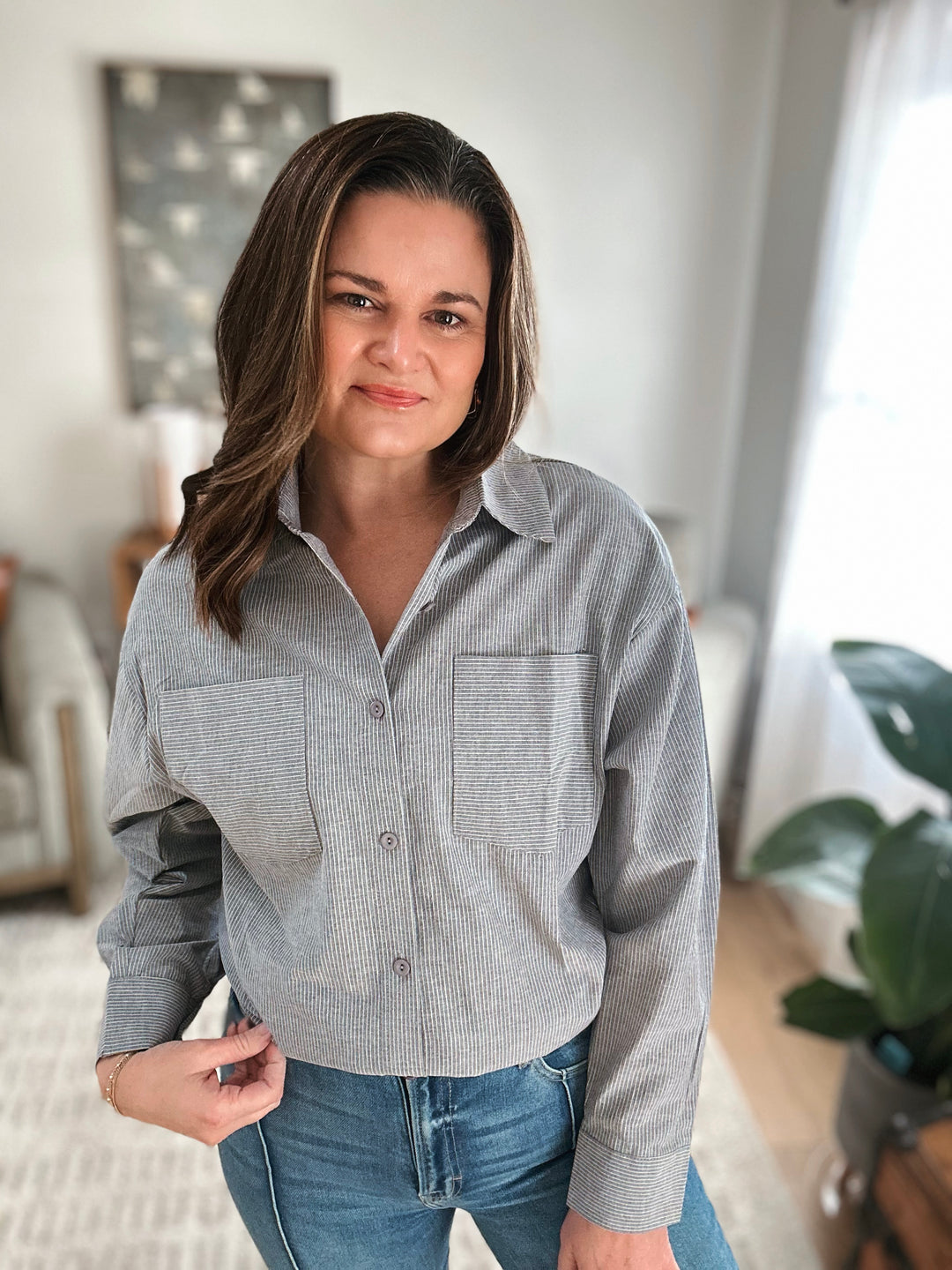 Woman wearing a gray striped shirt and blue jeans indoors.
