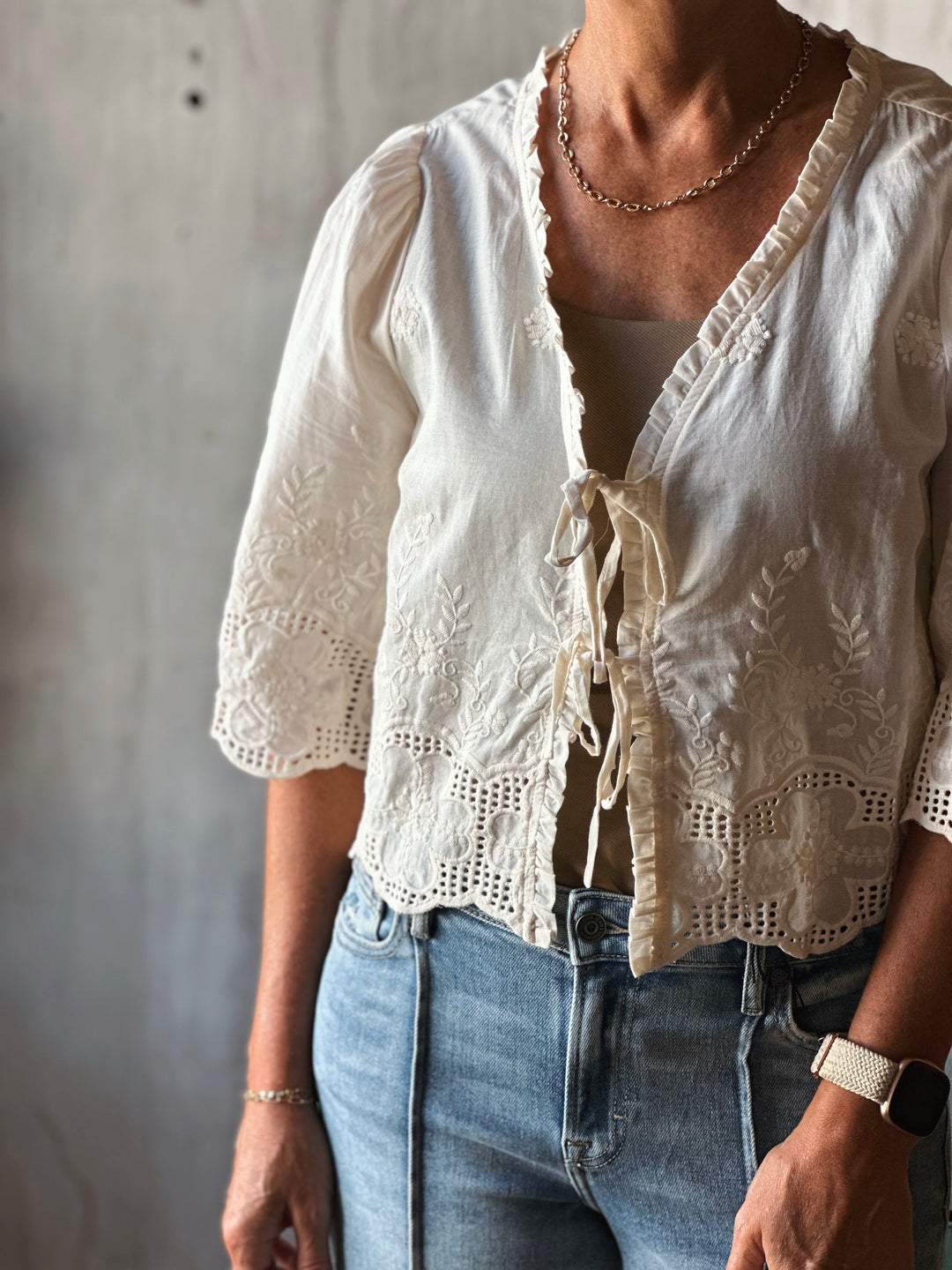 Person wearing a white lace top and blue jeans against a neutral background