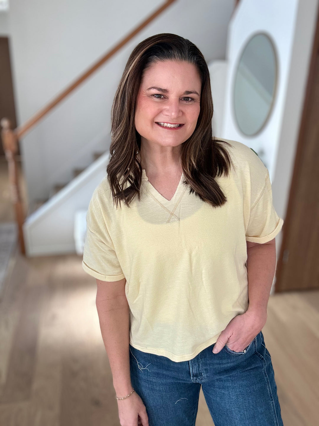 Woman wearing a light yellow t-shirt and blue jeans standing indoors.