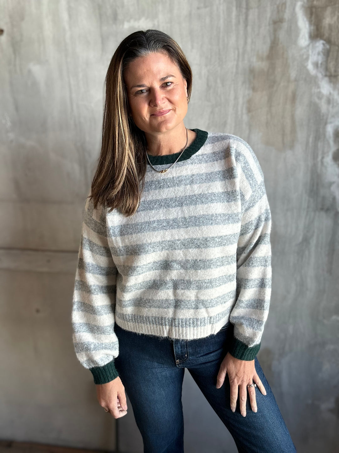 Woman wearing a gray and cream striped crewneck sweater with dark trim and jeans