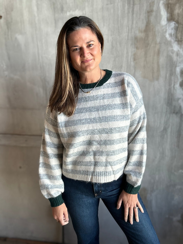 Woman wearing a gray and cream striped crewneck sweater with dark trim and jeans