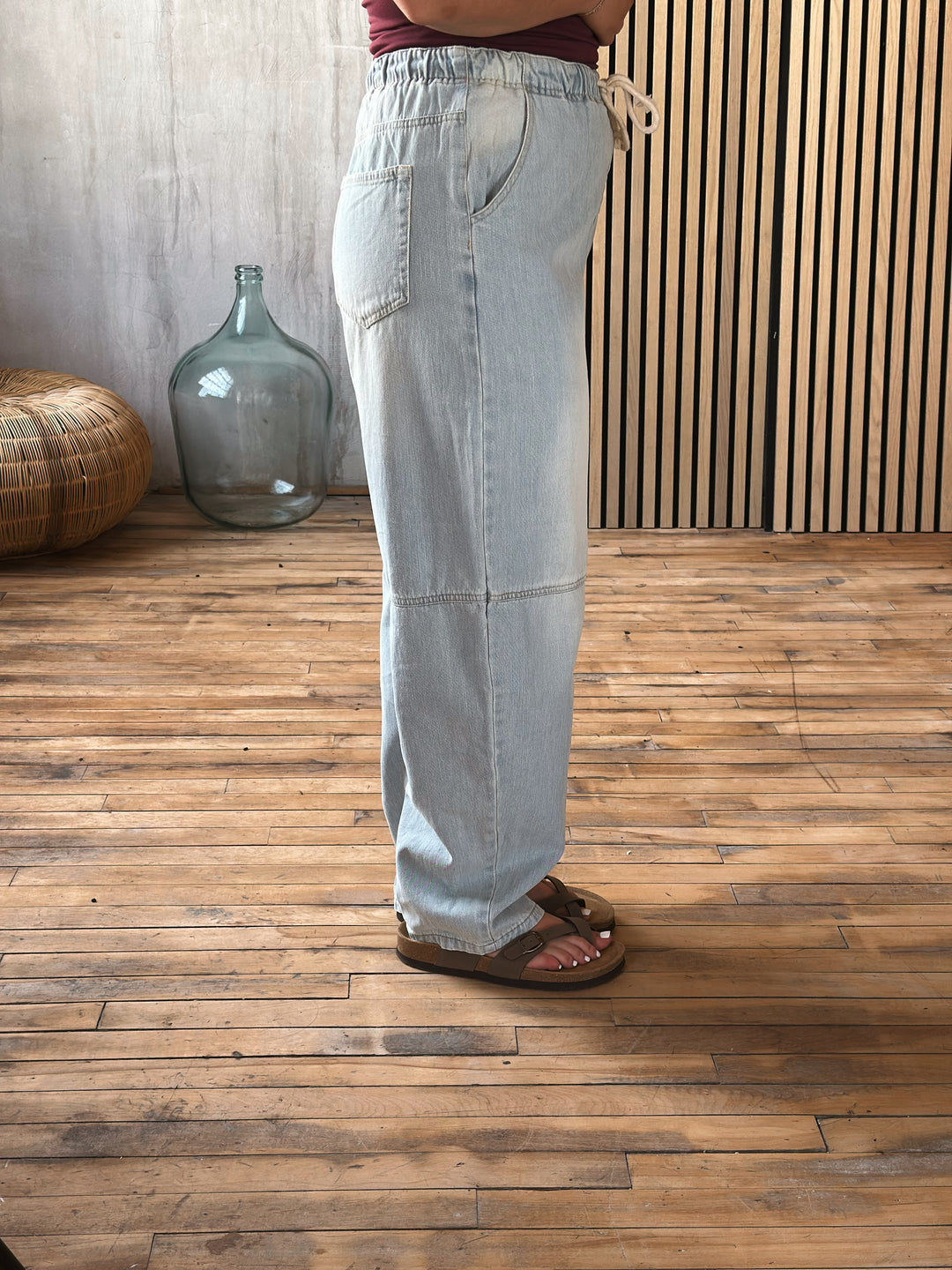 Light blue jeans worn by a person on a wooden floor with a textured wall background.