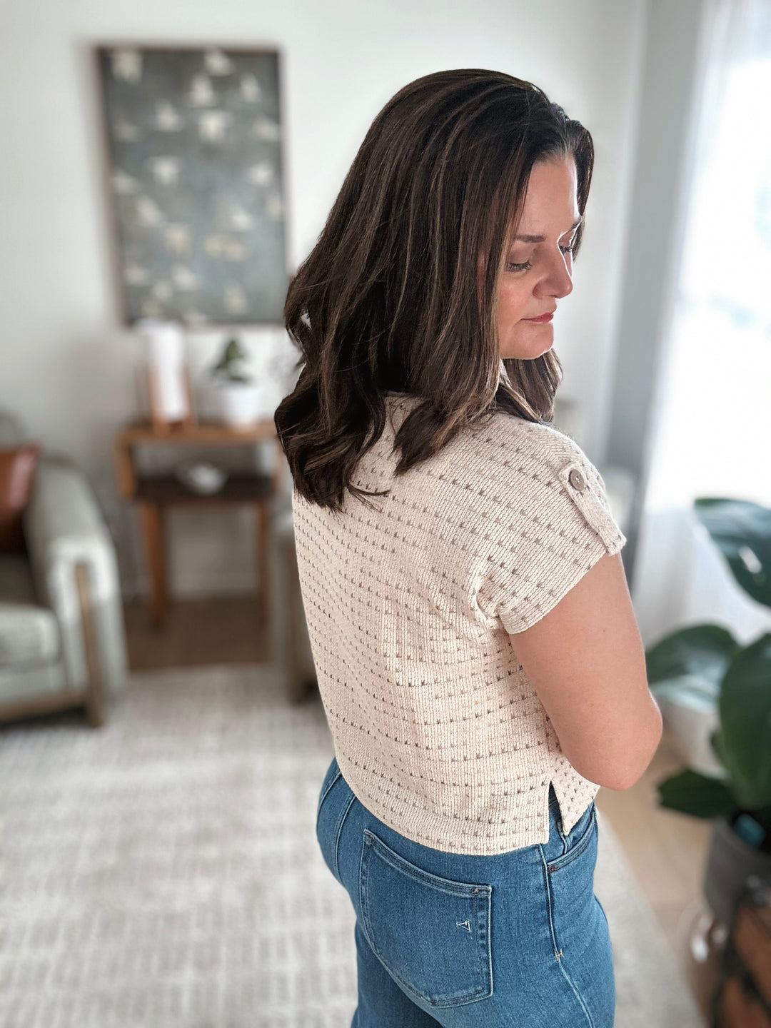 Woman wearing a beige short-sleeve top and blue jeans in a living room setting.