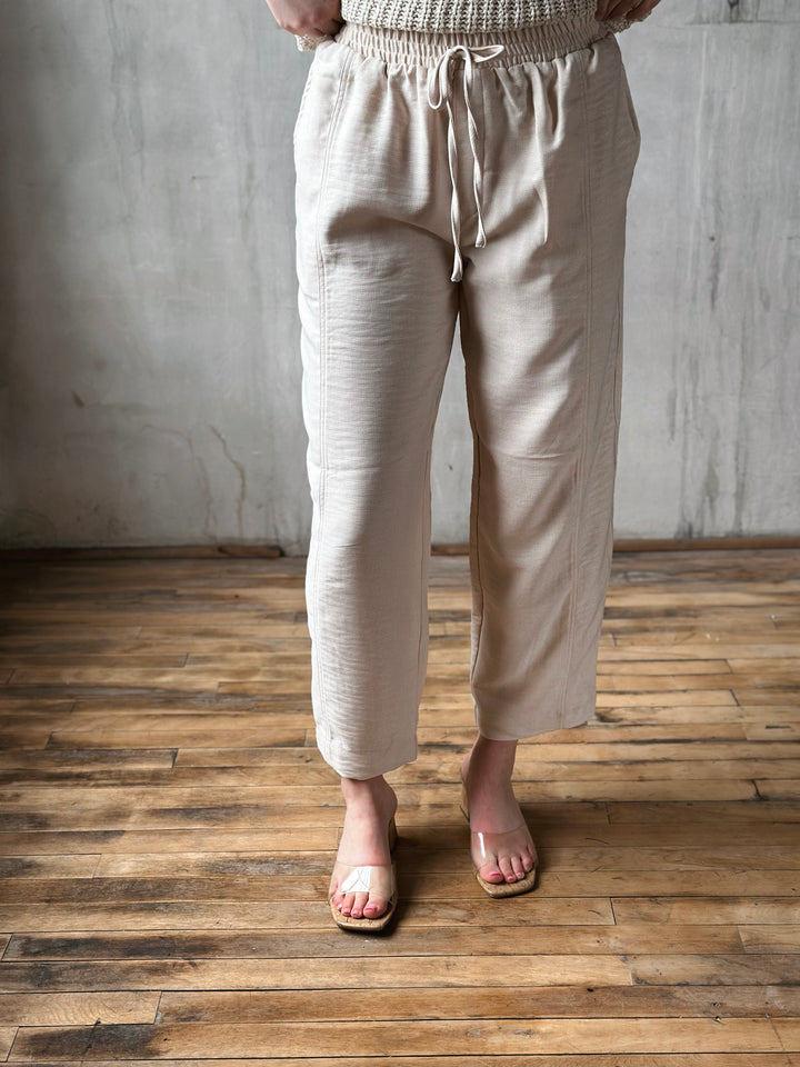 Person wearing beige pants standing on a wooden floor with a gray wall background