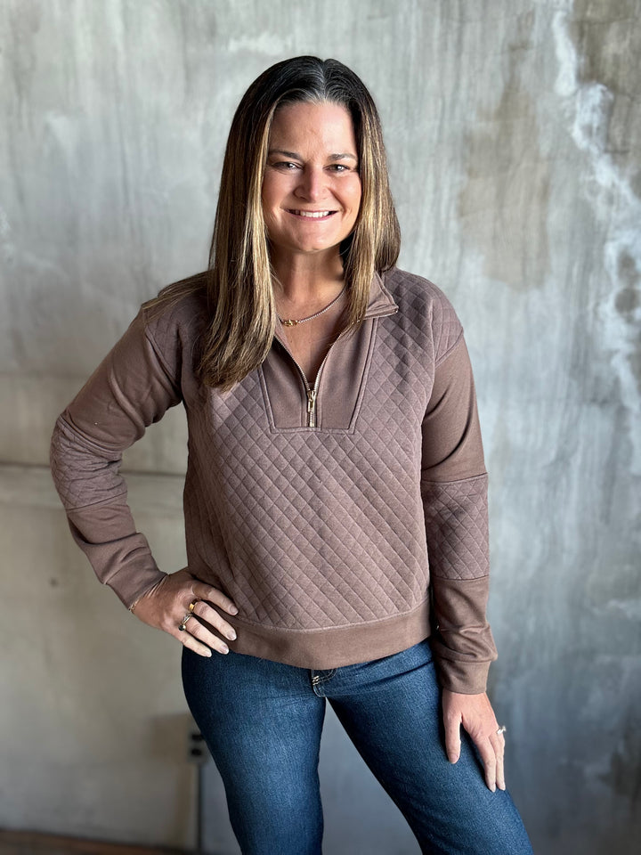 Woman wearing a mocha brown quilted half-zip pullover with dark jeans