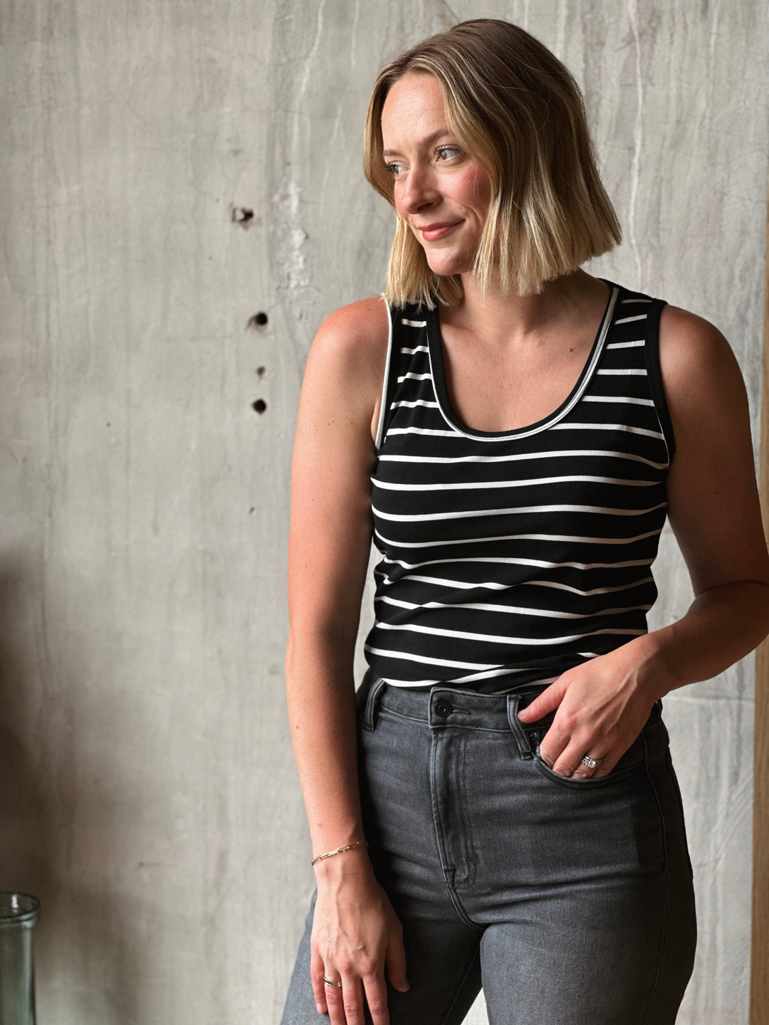 Woman wearing a black and white striped tank top against a concrete wall.