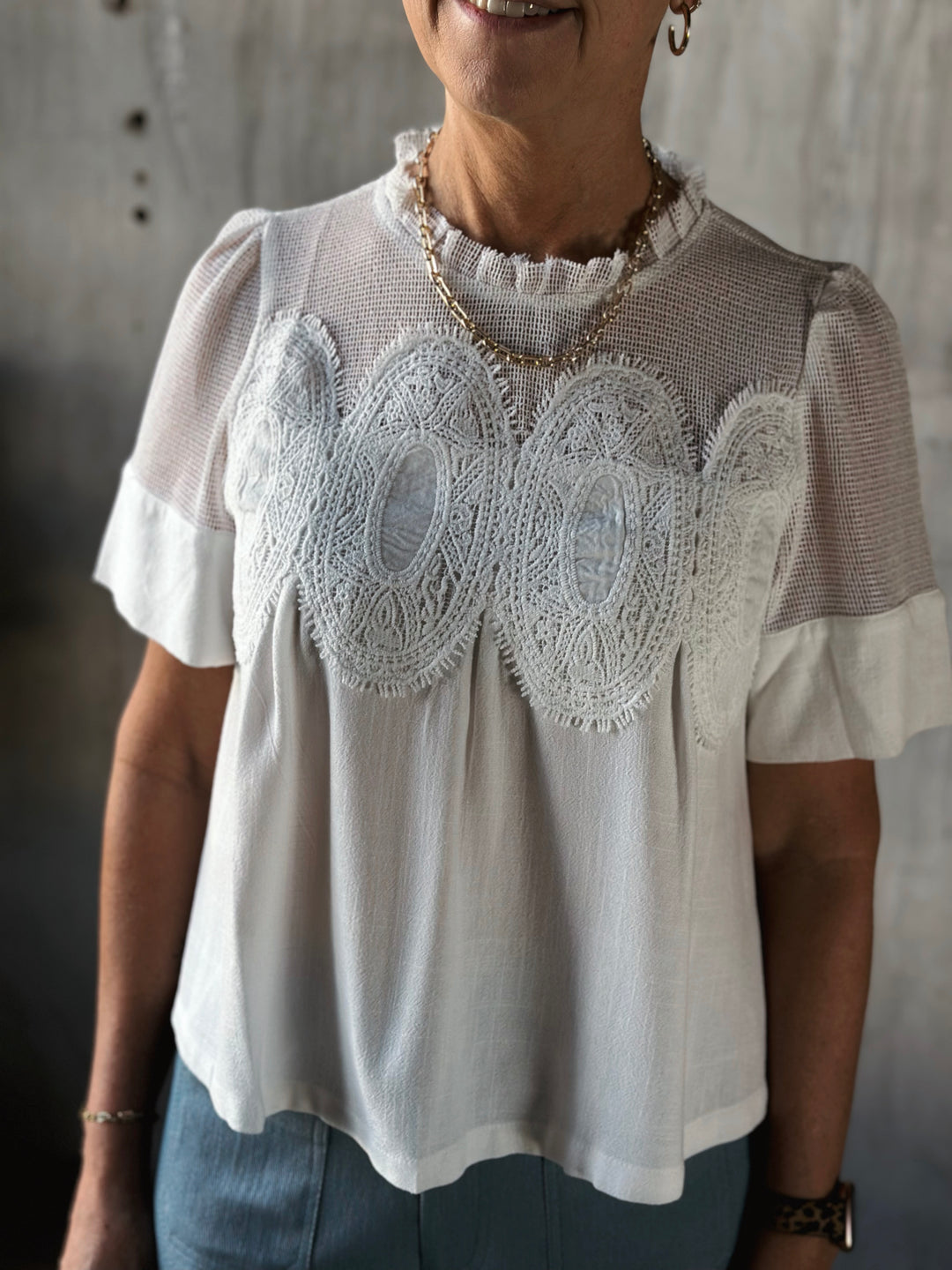 Woman wearing a white blouse with lace details against a neutral background