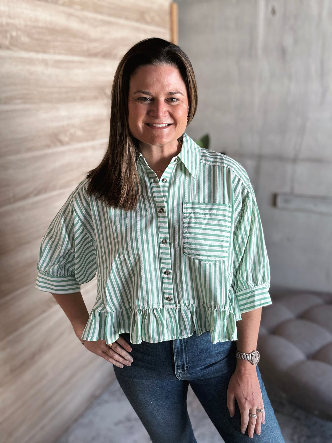 Woman wearing a green and white striped shirt with a ruffle hem at the bottom of the shirt and buttons down the middle.